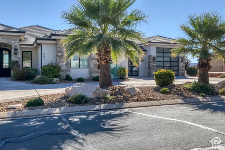Stucco and stone exterior with a tile roof, featuring a glass panel garage door and xeriscape landscaping