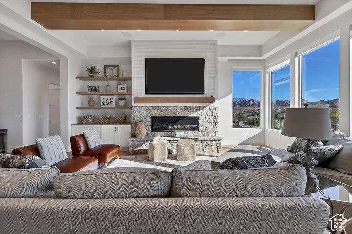 Expansive windows offering mountain scenery, wood-finish ceiling beams, stone fireplace, built-in shelving, and wood-finish flooring