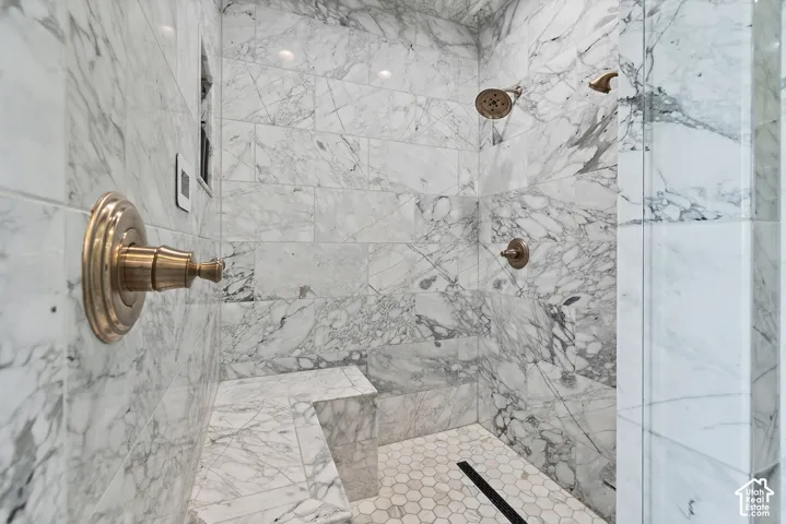 Shower with full-height marble-finish tile, integrated shower bench, dual shower heads, and hexagonal mosaic tile flooring