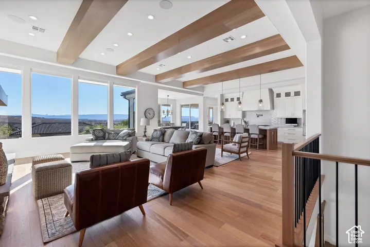 Open-concept living space featuring wood-finish flooring, exposed ceiling beams, recessed lighting, and large windows