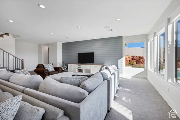 Recessed lighting, light gray carpeting, floor-to-ceiling windows, and a shiplap accent wall with a built-in media console