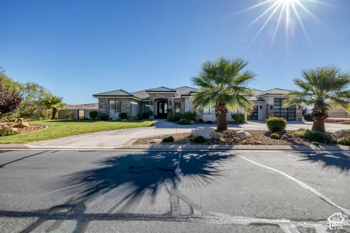 Stone and stucco exterior, arched entry, multiple garage bays with frosted glass doors, established landscaping, and palm trees