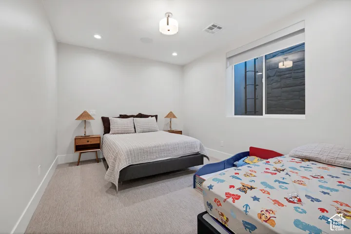 Versatile secondary bedroom featuring neutral carpeting, abundant natural light from large windows, and space to accommodate multiple sleeping arrangements with built-in ceiling lighting