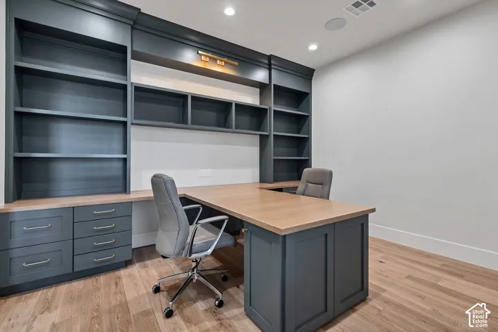 Built-in cabinetry with integrated shelving, L-shaped wood-finish desktop, wood-finish flooring, and recessed lighting