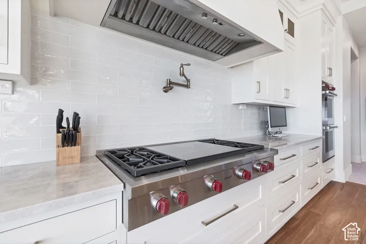 Stainless steel range with red knob accents, white shaker-style cabinetry, light-toned stone countertops, white subway tile backsplash, and wood-finish flooring