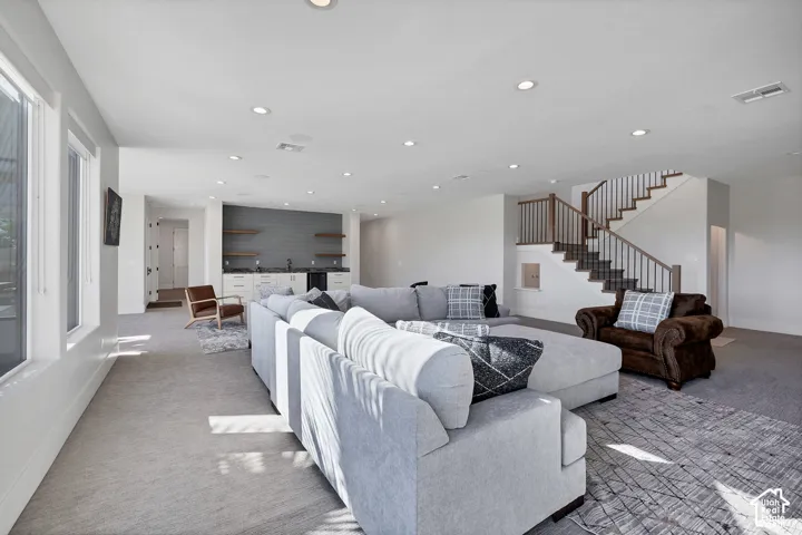 Expansive entertainment space featuring recessed lighting, a built-in wet bar with open shelving, and a prominent staircase with wood newel posts and railings