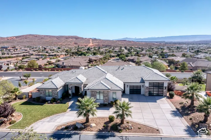 Stone and stucco exterior with a tiled roof, a concrete driveway, and integrated garage doors