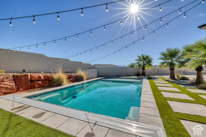 Private backyard featuring a swimming pool, string lighting, and landscape elements including palm trees and decorative rock