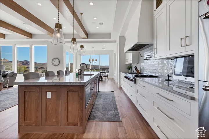 Gourmet kitchen featuring a large island with wood-finish paneling, white shaker cabinetry, stainless steel appliances, and a textured tile backsplash