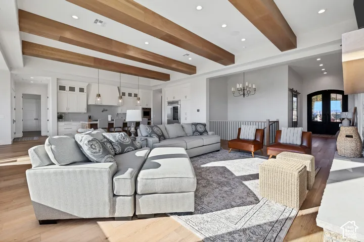 Vaulted ceilings with exposed wood beams, recessed lighting, wood-finish flooring, white cabinetry, and double arched entry doors