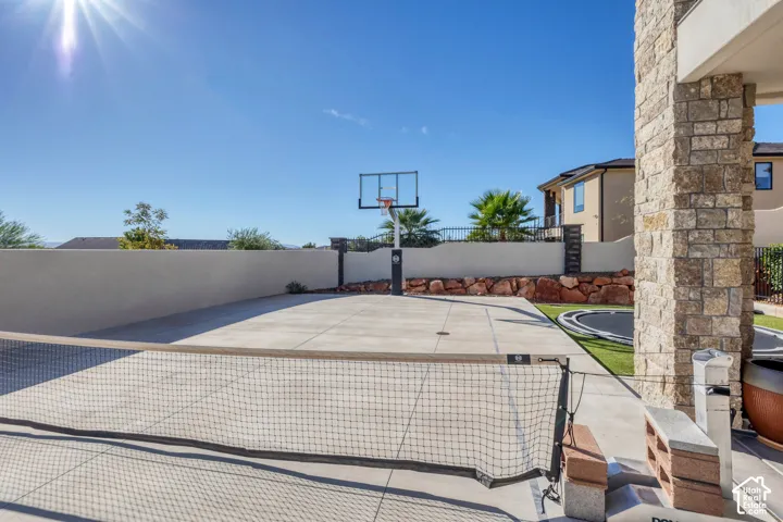 Concrete sport court with a basketball hoop and a tennis net, surrounded by a stucco privacy wall and a stone-clad column