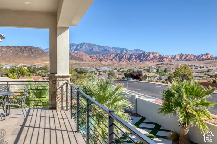 Spacious balcony with stone-clad pillars, sleek horizontal metal railings, tile flooring, and distant mountain scenery