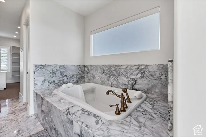 Built-in soaking tub with a bronze-finish faucet, surrounded by natural stone with distinct veining, and frosted window