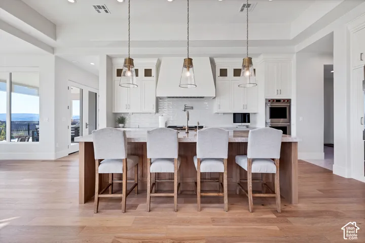 Expansive kitchen featuring wood-finish flooring, a central island with a stone countertop, white cabinetry, and stainless steel appliances