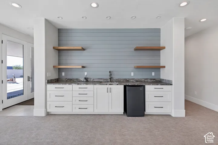 Wet bar with white cabinetry, dark countertops, built-in beverage refrigerator, and open wood-finish shelving