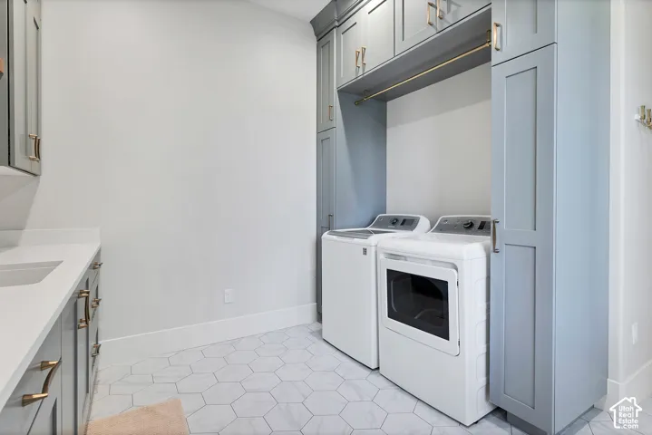 White hexagonal floor tiling with veining, light gray cabinetry with gold-tone hardware, white countertop with integrated sink, and a gold-tone hanging rod