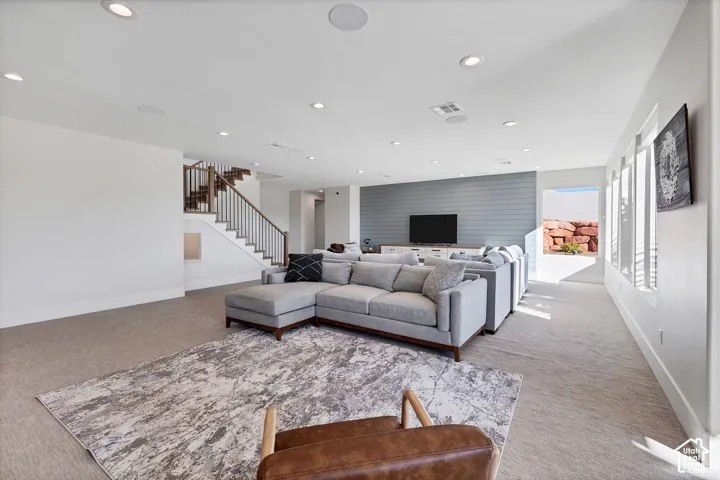 Spacious open-concept living area featuring a wood-finish staircase with metal spindles, recessed lighting, and a shiplap accent wall