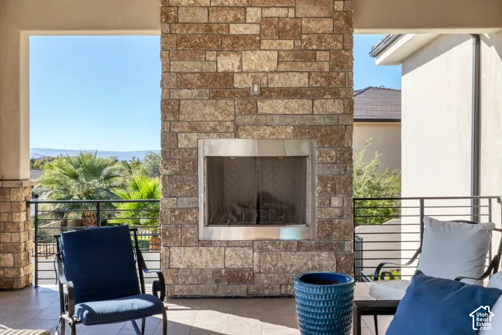 Covered outdoor patio featuring a stone-clad fireplace with a stainless steel insert, tile flooring, and metal railing