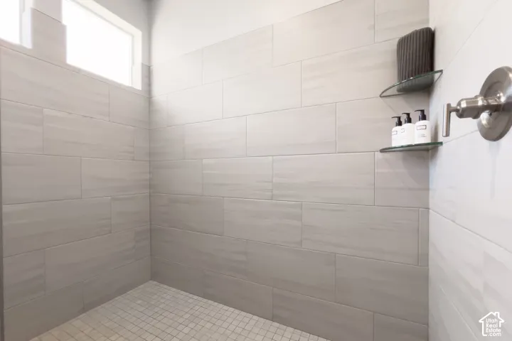 Tiled shower enclosure featuring light-toned rectangular wall tiles, a mosaic tile floor, and a brushed nickel shower fixture