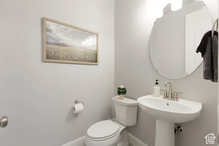 Pedestal sink with a brushed nickel faucet, circular mirror, and wall-mounted light fixture