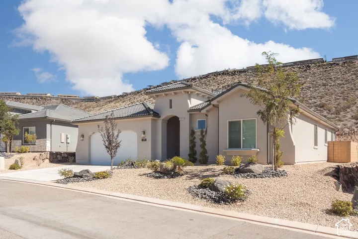 Stucco exterior with a tiled roof, arched entry, two-car garage, and desert-style landscaping