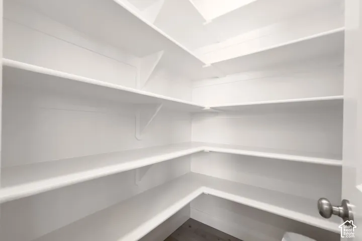 Walk-in pantry with multiple white built-in shelves and wood-finish flooring