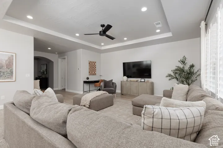 Recessed lighting illuminates the tray ceiling with a matte black ceiling fan
