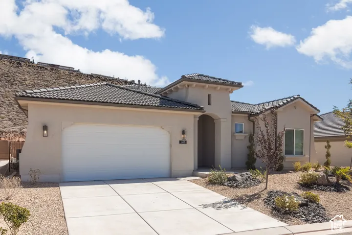 Stucco exterior with a tile roof, concrete driveway, attached garage, and a landscaped front yard featuring decorative rock and plantings