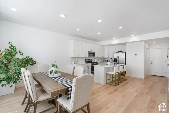 Open-concept living area featuring light wood-finish flooring, recessed lighting, white kitchen cabinetry, stainless steel appliances, and a kitchen island with seating