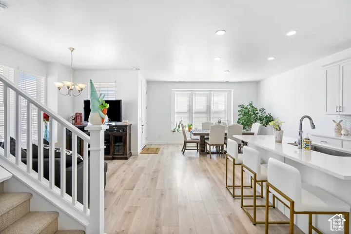 Open-concept living area with wood-finish flooring, recessed lighting, and a white kitchen island featuring a stainless steel sink and a gooseneck faucet