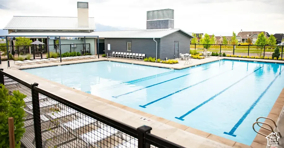 Community swimming pool with dedicated lap lanes, surrounded by concrete decking, featuring a shaded lounge area, and a building with horizontal siding