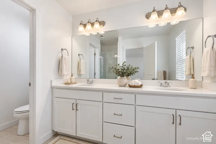 Dual vanity with white cabinetry, integrated sinks, white countertops, and a large wall-mounted mirror with overhead lighting