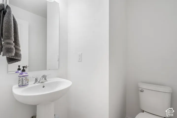 Pedestal sink with chrome faucet, wall-mounted mirror, and white toilet