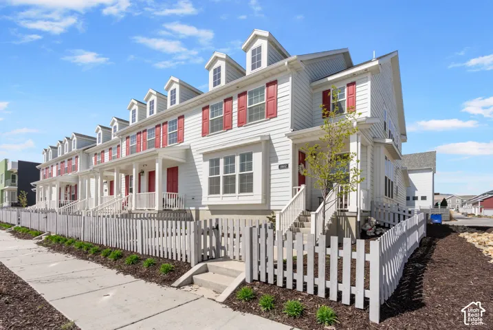White siding exterior with red shutters, dormer windows, covered entry porch, and a white picket fence