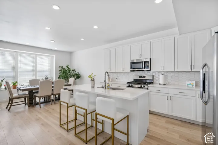 Open-concept kitchen and dining area featuring light wood-finish flooring, white cabinetry, integrated stainless steel appliances, and a kitchen island with seating