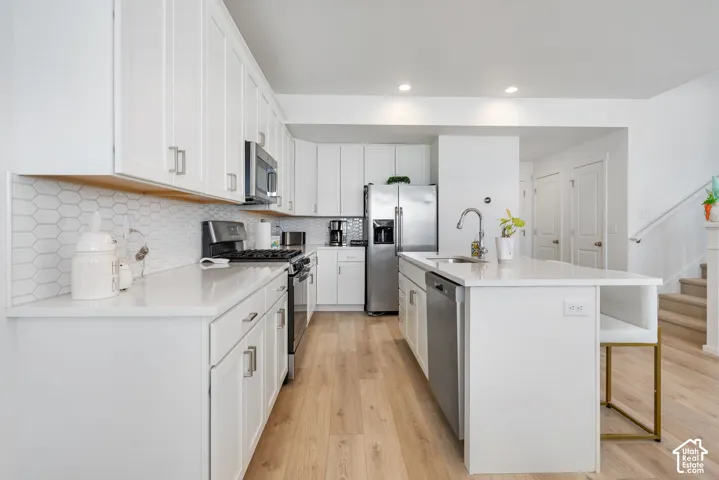 Contemporary kitchen featuring white cabinetry, stainless steel appliances, wood-finish flooring, white countertops, and a white hexagonal tile backsplash