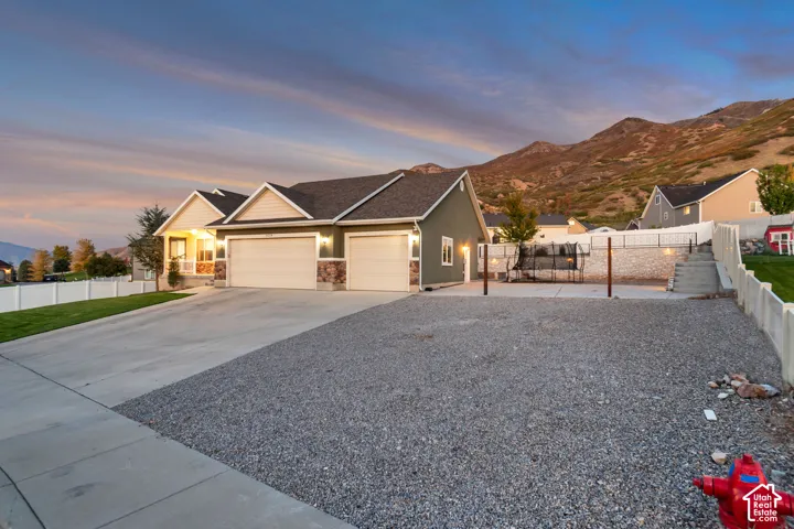 Three-car garage with concrete driveway, light green siding, stone accents, and front porch