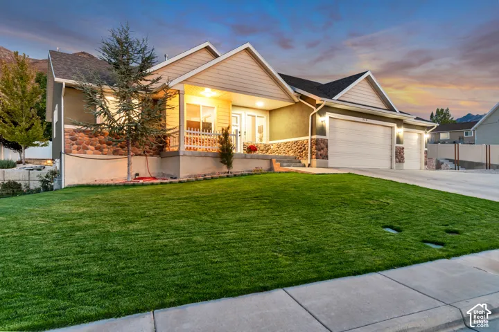 Expansive front lawn, stone and stucco exterior, covered front porch, three-car garage, and concrete driveway