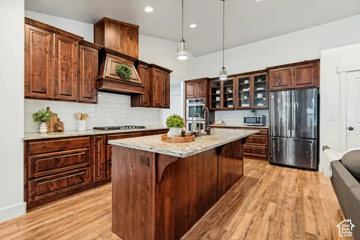 Kitchen featuring wood-finish flooring, dark wood cabinetry, light-toned countertops, a subway tile backsplash, and stainless steel appliances
