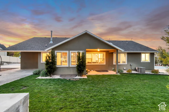 Expansive green lawn with a concrete patio, covered outdoor living space, and a paved driveway