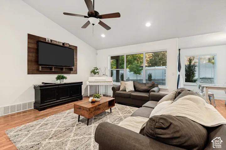 Vaulted ceiling with a ceiling fan and recessed lighting, wood-finish flooring, and large windows with blinds