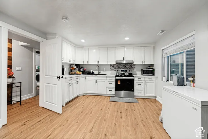 U-shaped kitchen with wood-finish flooring, white cabinetry, stainless steel appliances, and a tiled backsplash