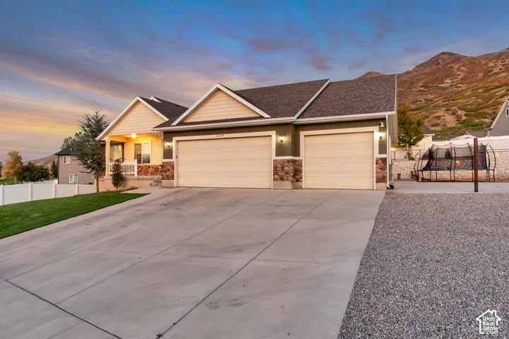 Exterior featuring a three-car garage, stone and siding facade, covered entry, and a prominent mountain backdrop