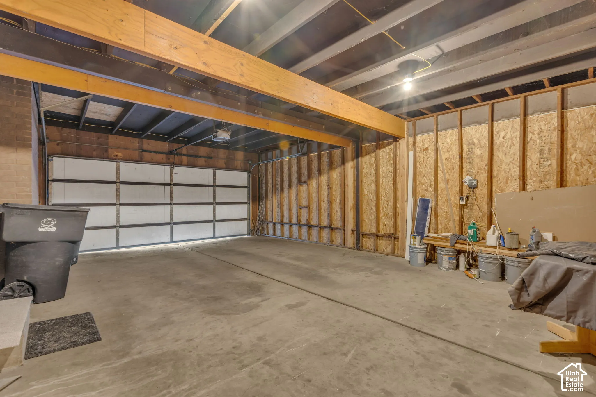 Unfinished garage space with a concrete floor, exposed wooden ceiling joists, and a sectional garage door