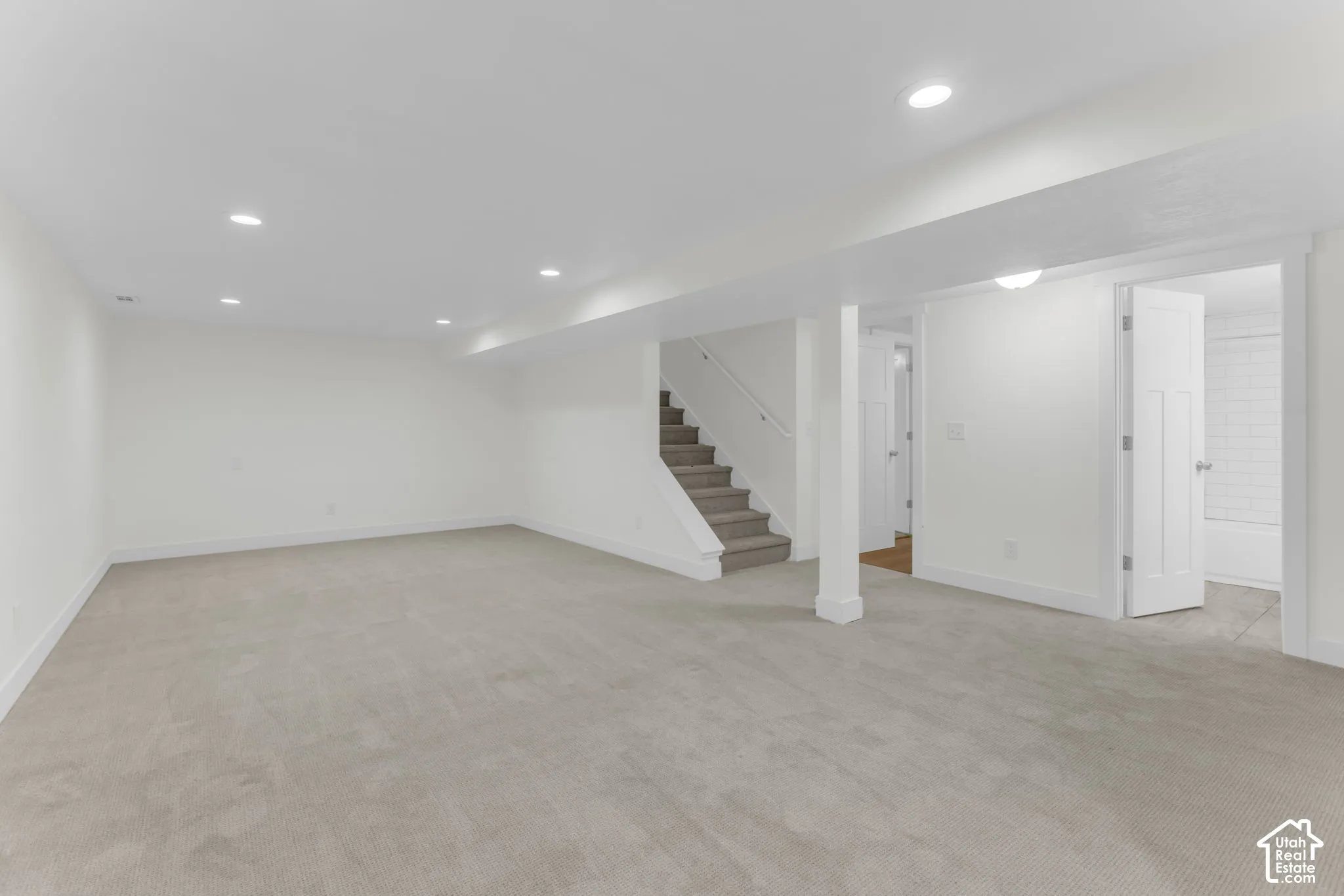 Expansive carpeted area with recessed lighting, a staircase with carpeting, and white paneled doors