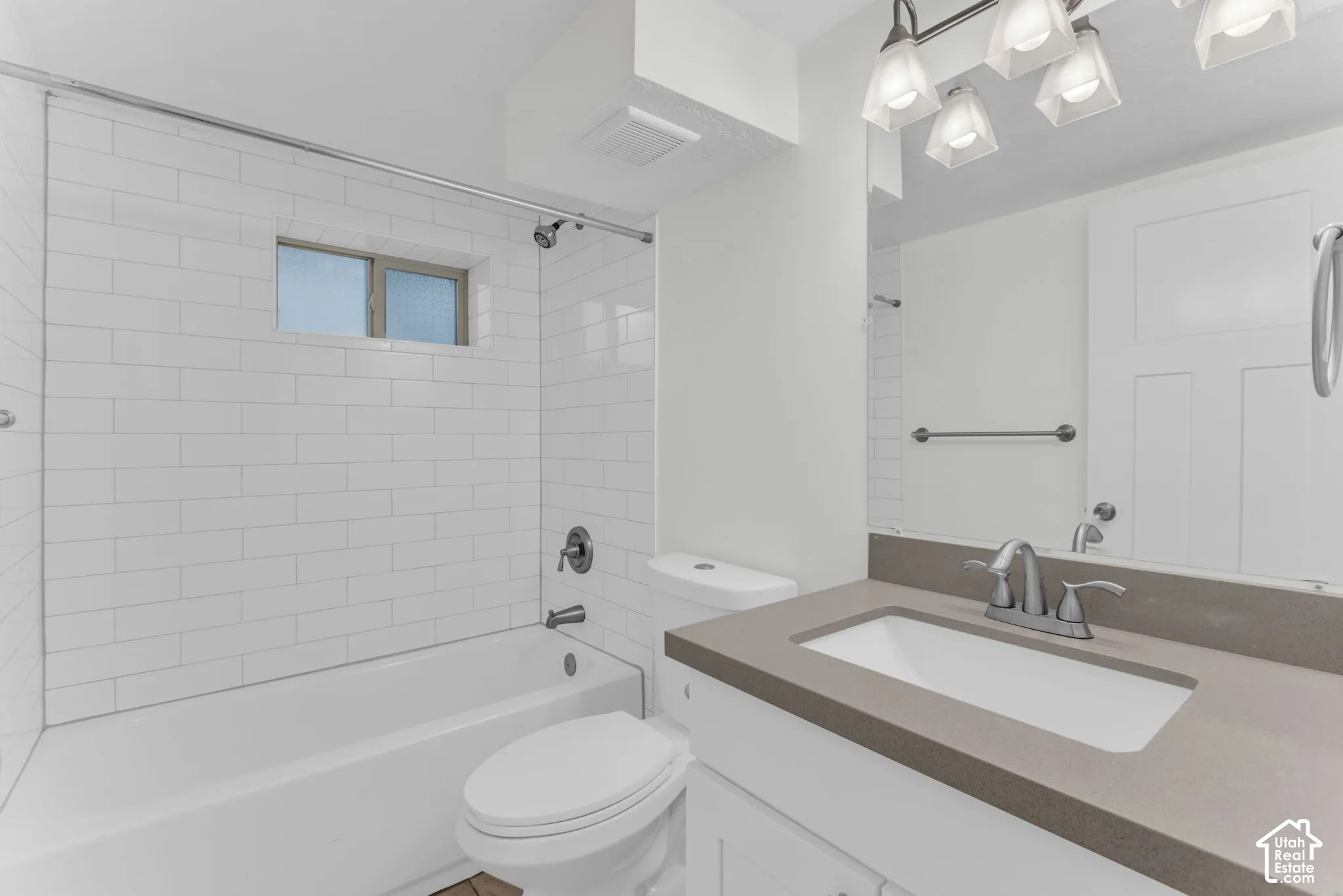 Bathroom featuring a white subway tile tub surround, built-in bathtub, window, vanity with an integrated sink, and overhead lighting