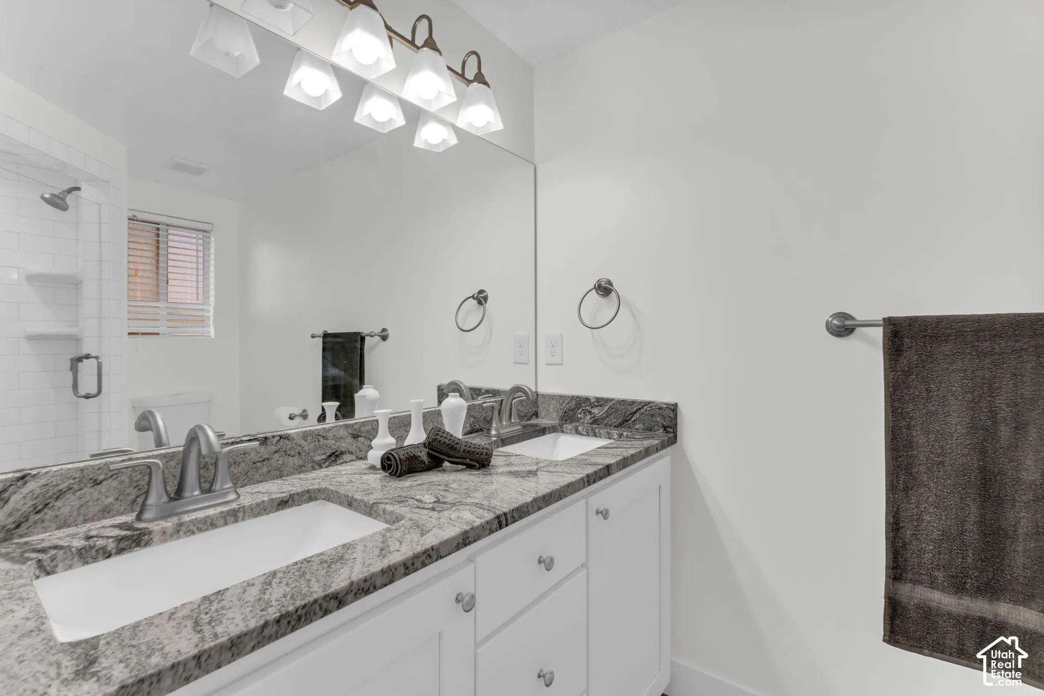 Dual vanity with integrated sinks, granite countertop, white cabinetry, and brushed nickel hardware