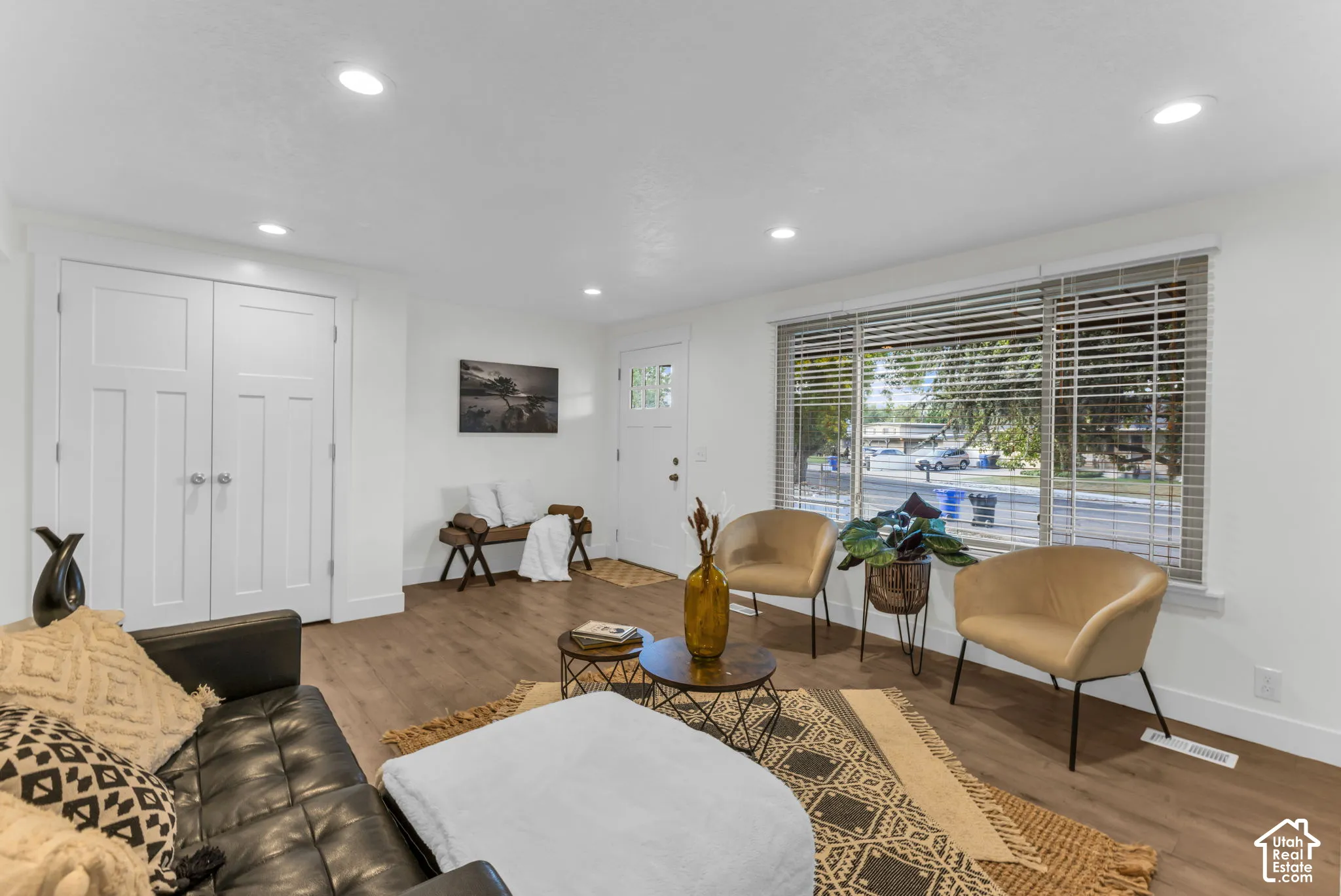 Recessed lighting, wood-finish flooring, white trim details, and a large window with horizontal blinds