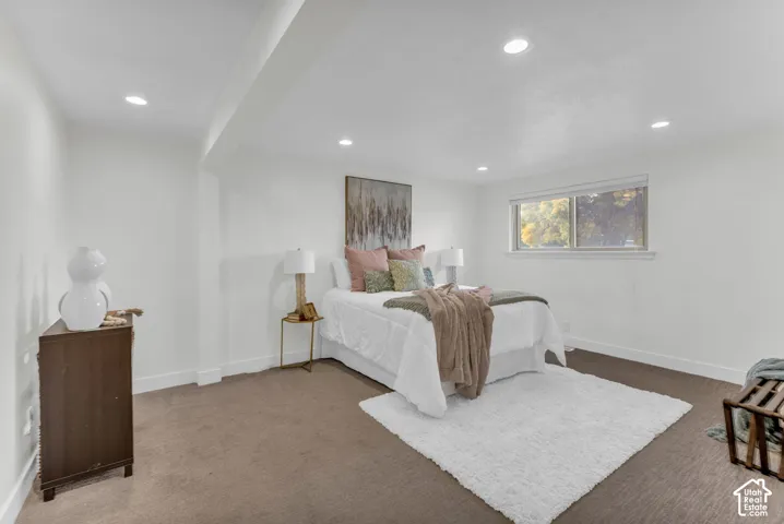 Recessed lighting, white walls, brown carpeting, and a window with natural light