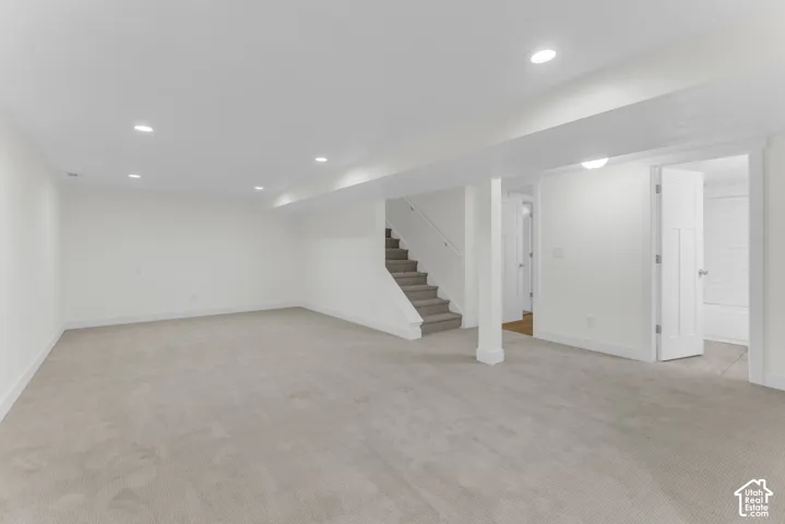 Expansive carpeted area with recessed lighting, a staircase with carpeting, and white paneled doors